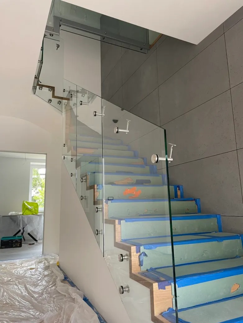 Szklana balustrada zamontowana na schodach w trakcie zabezpieczania, widoczne taśmy malarskie i folia ochronna.