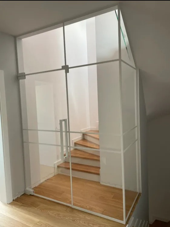 Szklana zabudowa schodów z białymi profilami, widok na drewniane schody i białe ściany.