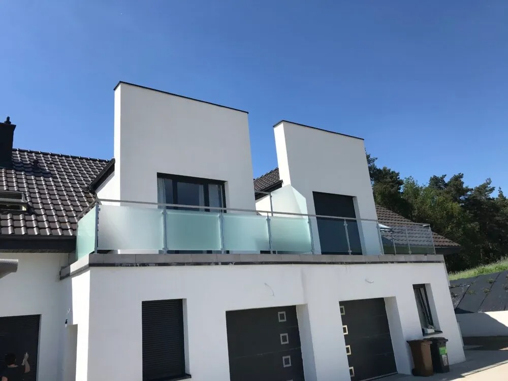 Nowoczesny dom z białymi ścianami i balkonem zabezpieczonym balustradą ze szkła mrożonego, widok z dołu w słoneczny dzień.