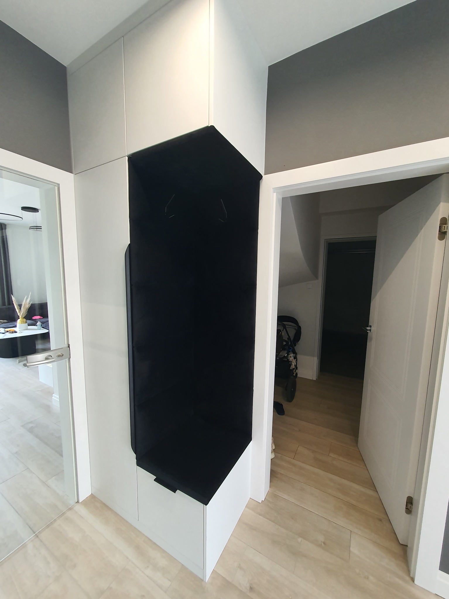 Nowoczesna zabudowa przedpokoju z biało-czarnym modułem na odzież wierzchnią, widok na salon i otwarte drzwi do pomieszczenia gospodarczego na poddaszu.