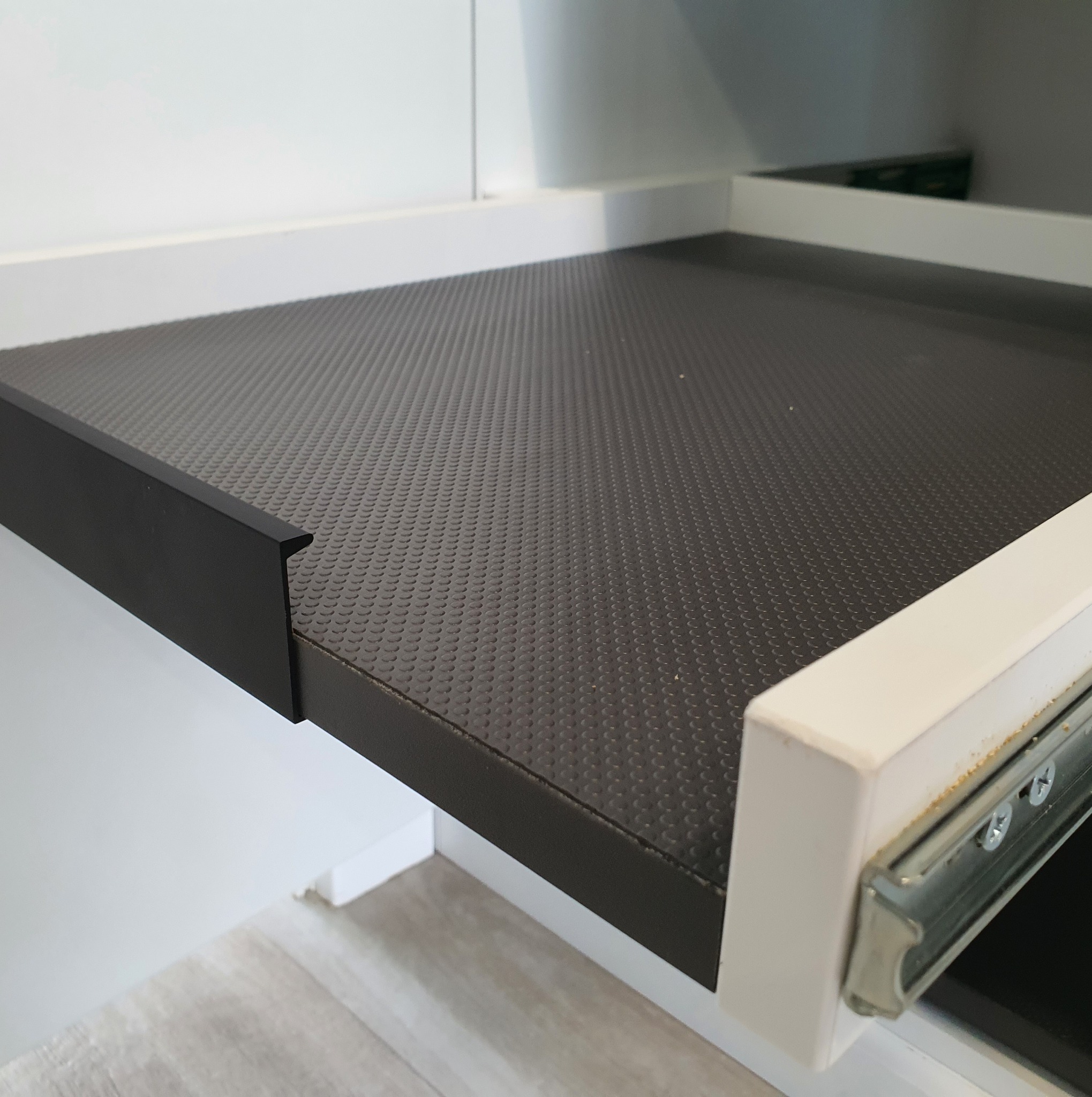 Wysuwana szuflada z antypoślizgową, gumowaną wykładziną wewnątrz szafki, widoczne prowadnice rolkowe.