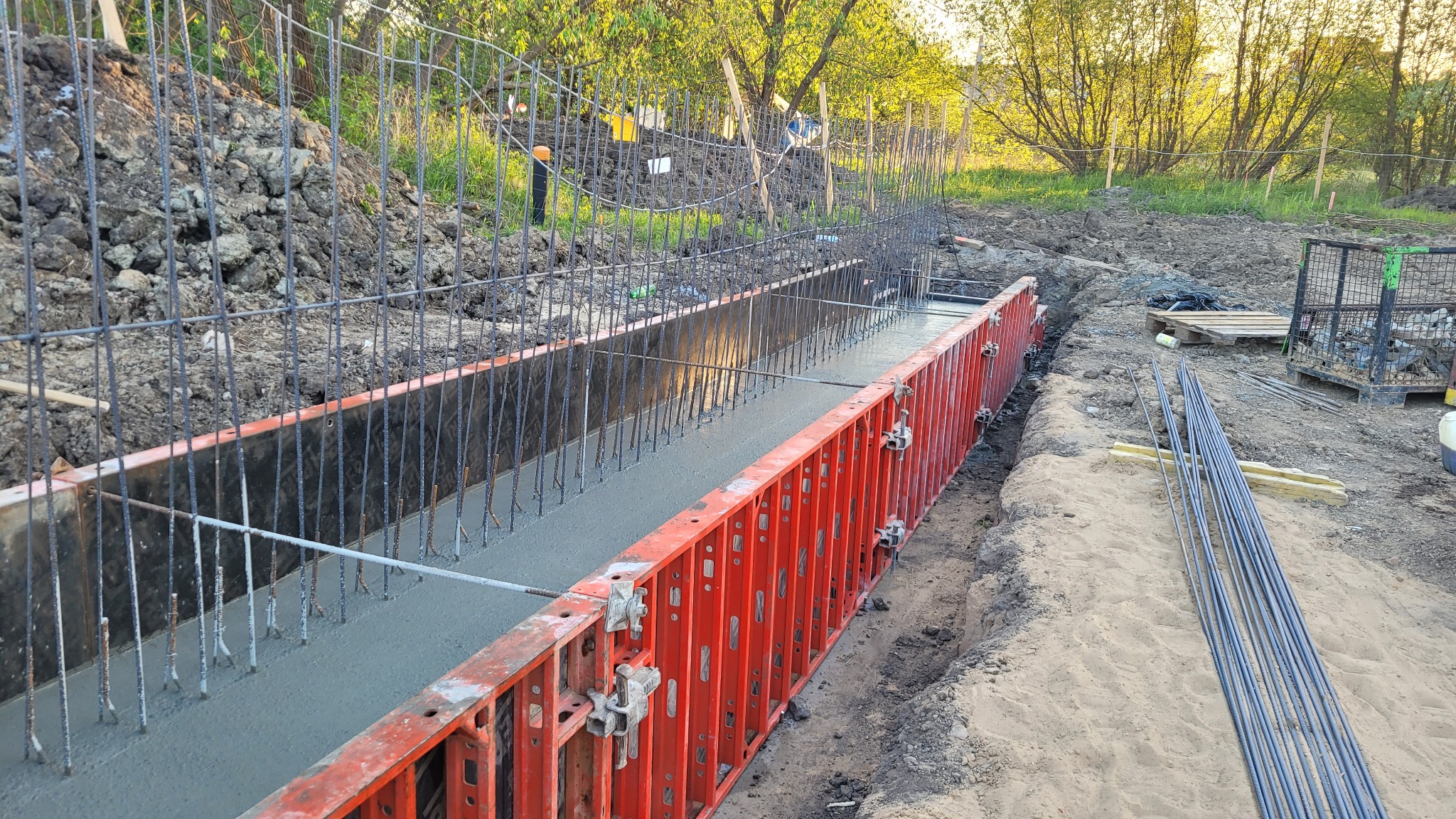 Wylany beton w szalunku zbrojonym prętami stalowymi, widok z boku na placu budowy w słoneczny dzień.
