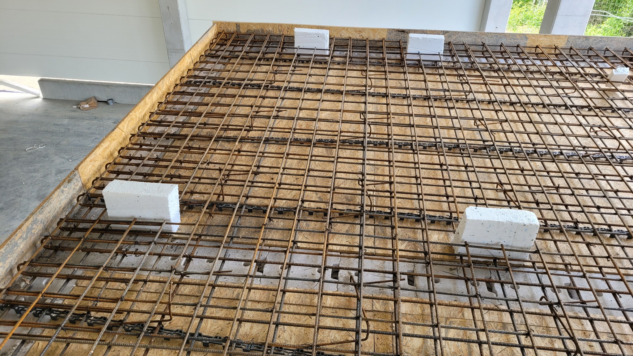 Siatka zbrojeniowa na deskowaniu, z dystansami z białego styropianu, przygotowana do zalania betonem.