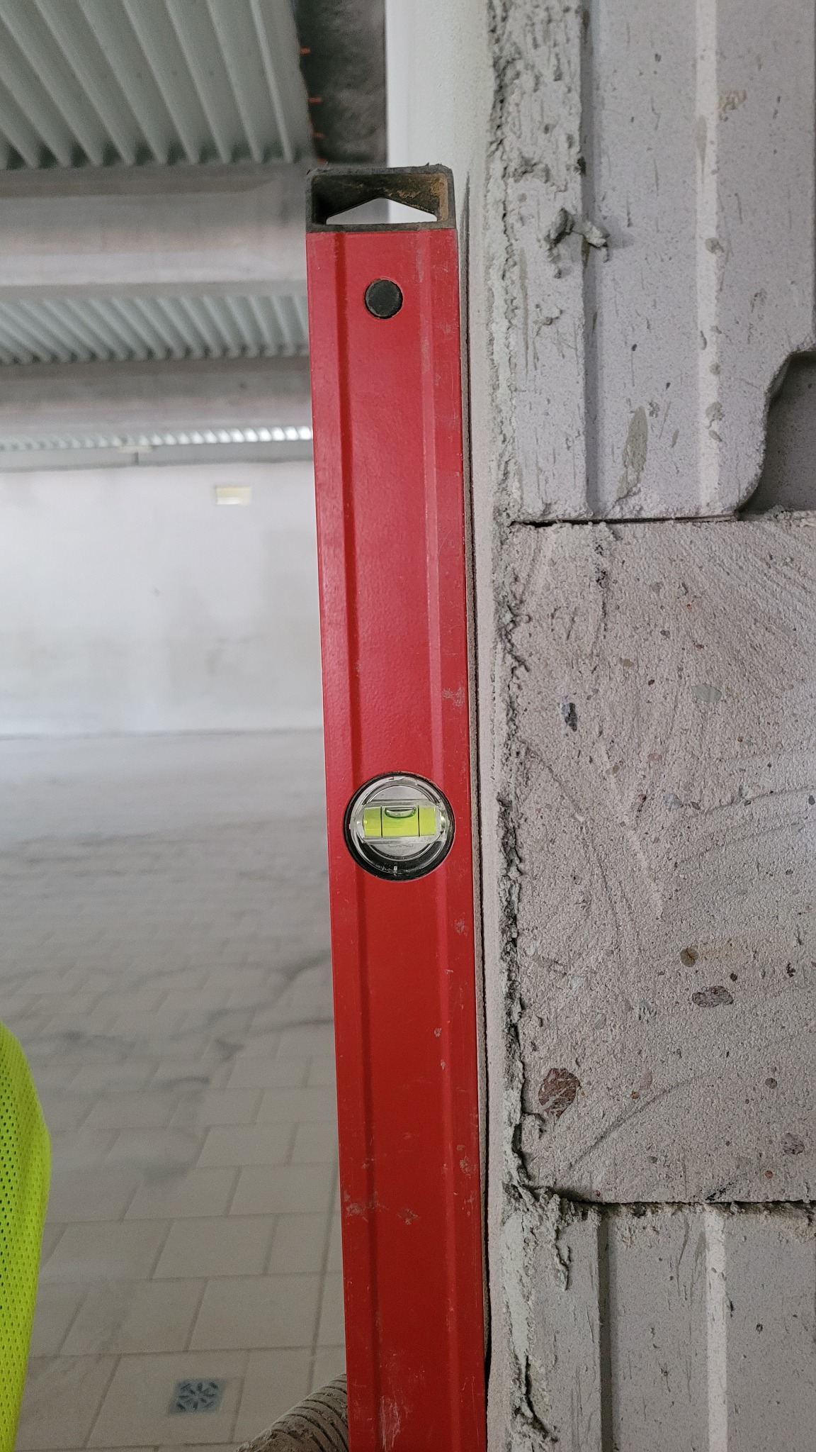 Czerwona poziomica przyłożona do surowej ściany z betonu komórkowego podczas prac budowlanych wewnątrz budynku.