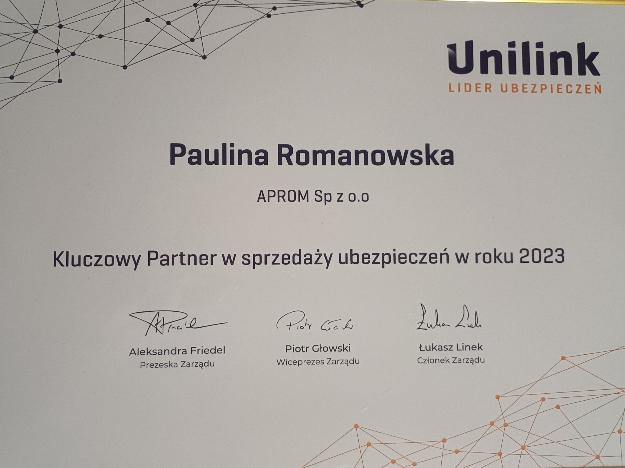 Dyplom dla Pauliny Romanowskiej z APROM Sp z o.o. jako Kluczowego Partnera w sprzedaży ubezpieczeń w roku 2023 od Unilink Lider Ubezpieczeń, podpisany przez Aleksandrę Friedel, Piotra Głowskiego...
