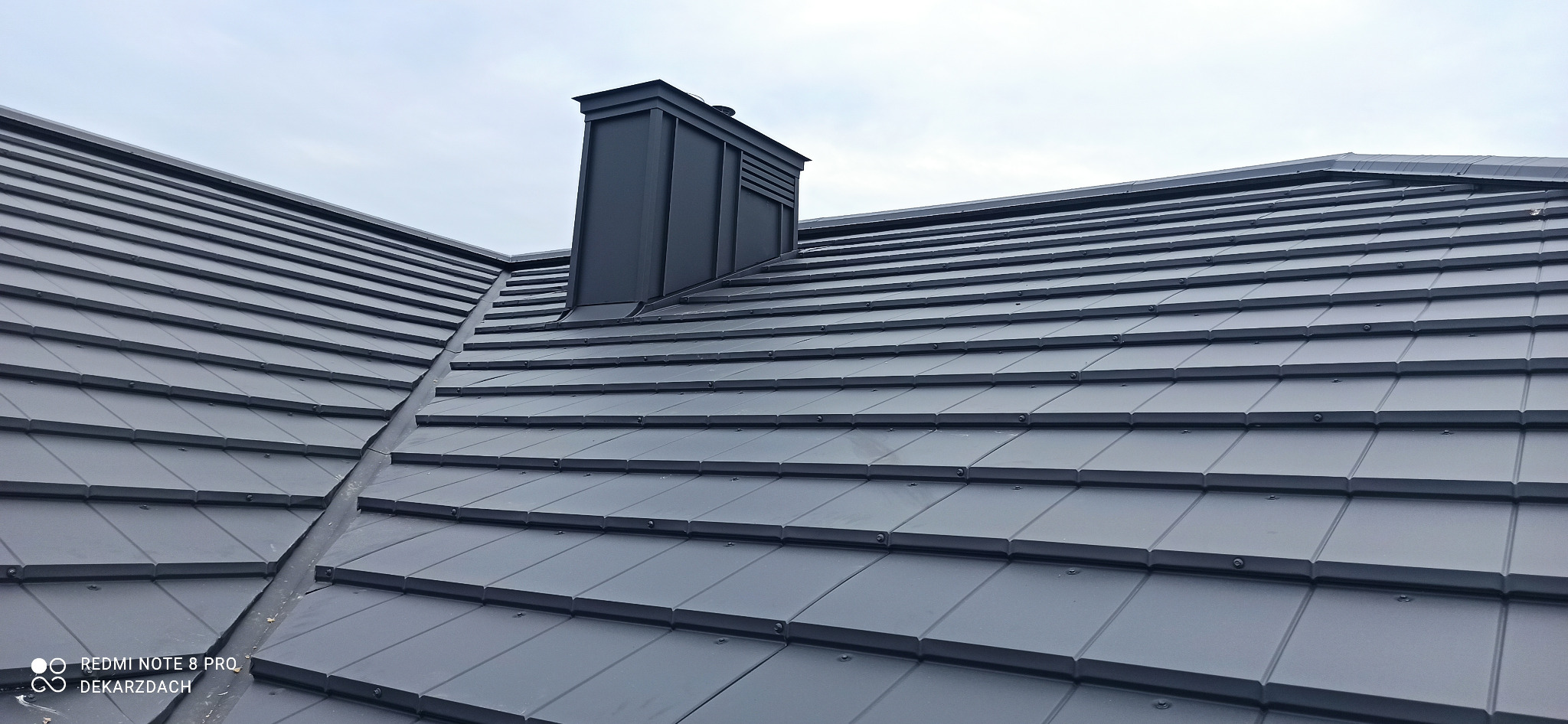 Nowoczesny dach z grafitowej blachy trapezowej z kominem, widok z góry, bez śladów użytkowania.