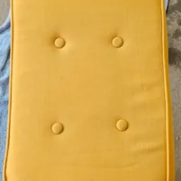 Ż&oacute;łta poduszka tapicerowana z guzikami po praniu, leżąca na niebieskiej szmatce. Widoczny efekt czystości po zabiegu.