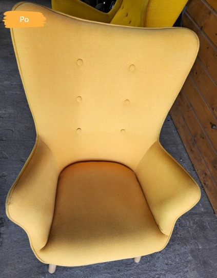 Żółty fotel typu uszak po czyszczeniu, widok z góry, z drewnianymi nogami i tapicerką z guzikami. Na zdjęciu widoczny napis 'Po'.