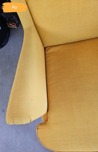 Żółty fotel tapicerowany po czyszczeniu, widok z góry. Odświeżony kolor i brak plam na tkaninie. Fragment stolika z butami w tle.