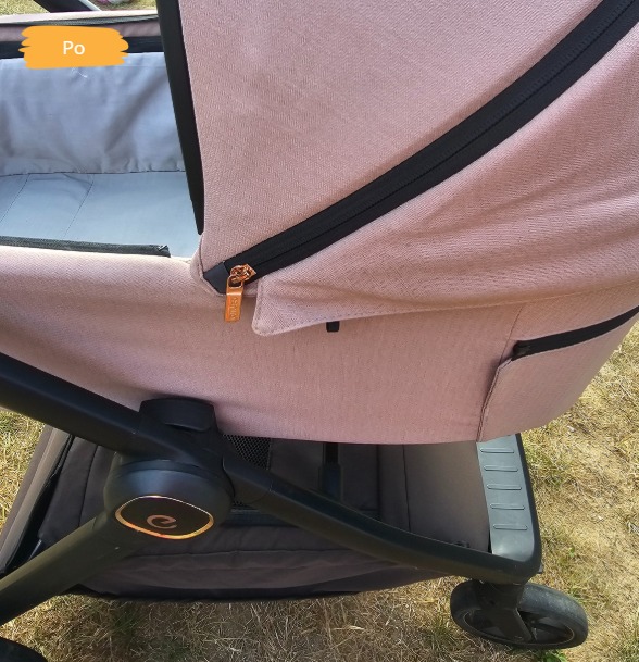 Wózek dziecięcy w odcieniach różu i czerni, widoczny z bliska, z napisem 'Po' sugerującym stan po czyszczeniu, na tle trawy.