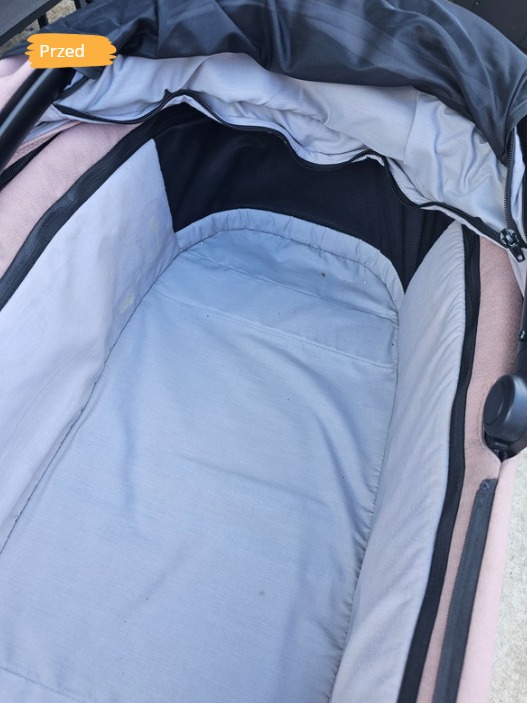 Wnętrze wózka dziecięcego w odcieniach szarości i różu, z widocznymi zabrudzeniami na poszyciu, w kadrze napis 'Przed'.