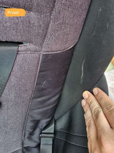 Zdjęcie fragmentu fotelika samochodowego z plamami i zabrudzeniami, z napisem 'Przed', ukazujące stan przed praniem tapicerki. Widoczna dłoń.