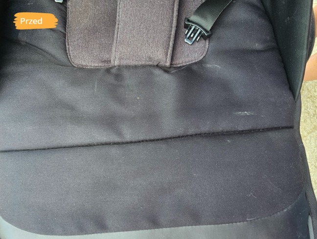 Ciemna tapicerka fotelika samochodowego z plamami, oznaczona jako 'Przed'. Widoczne pasy bezpieczeństwa i zapięcie.
