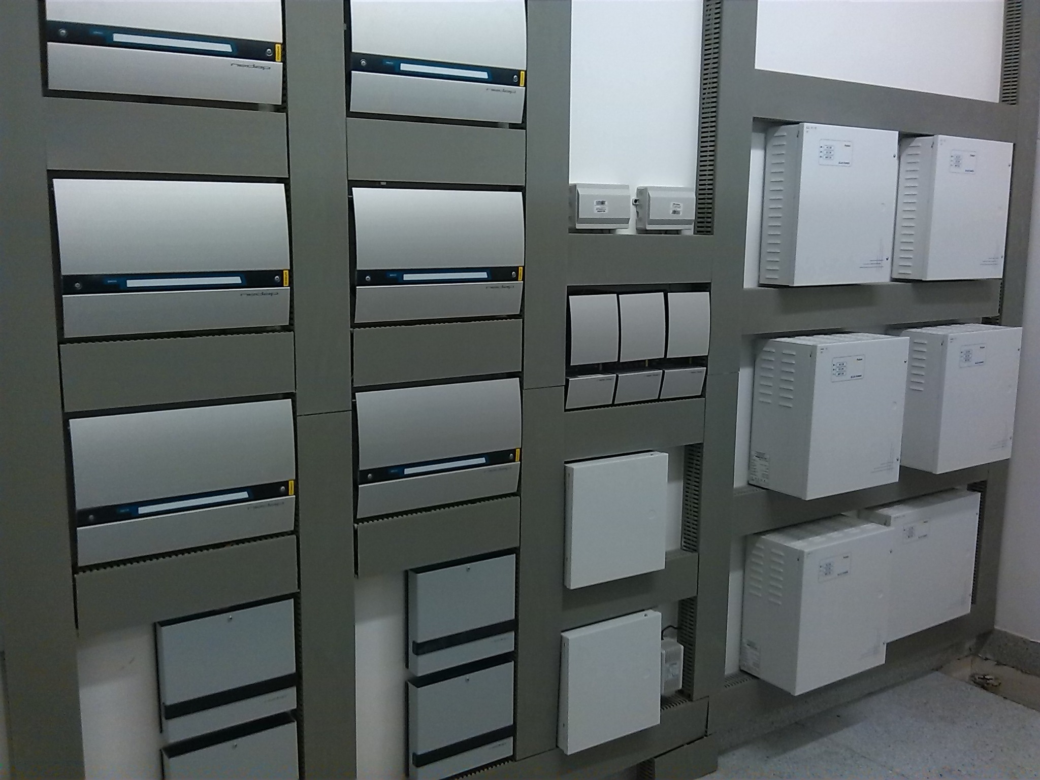 Rozbudowana instalacja elektryczna w szafie sterowniczej, widoczne moduły z listwami zaciskowymi i wyświetlaczami, szara obudowa, białe elementy, instalacja w obiekcie przemysłowym.