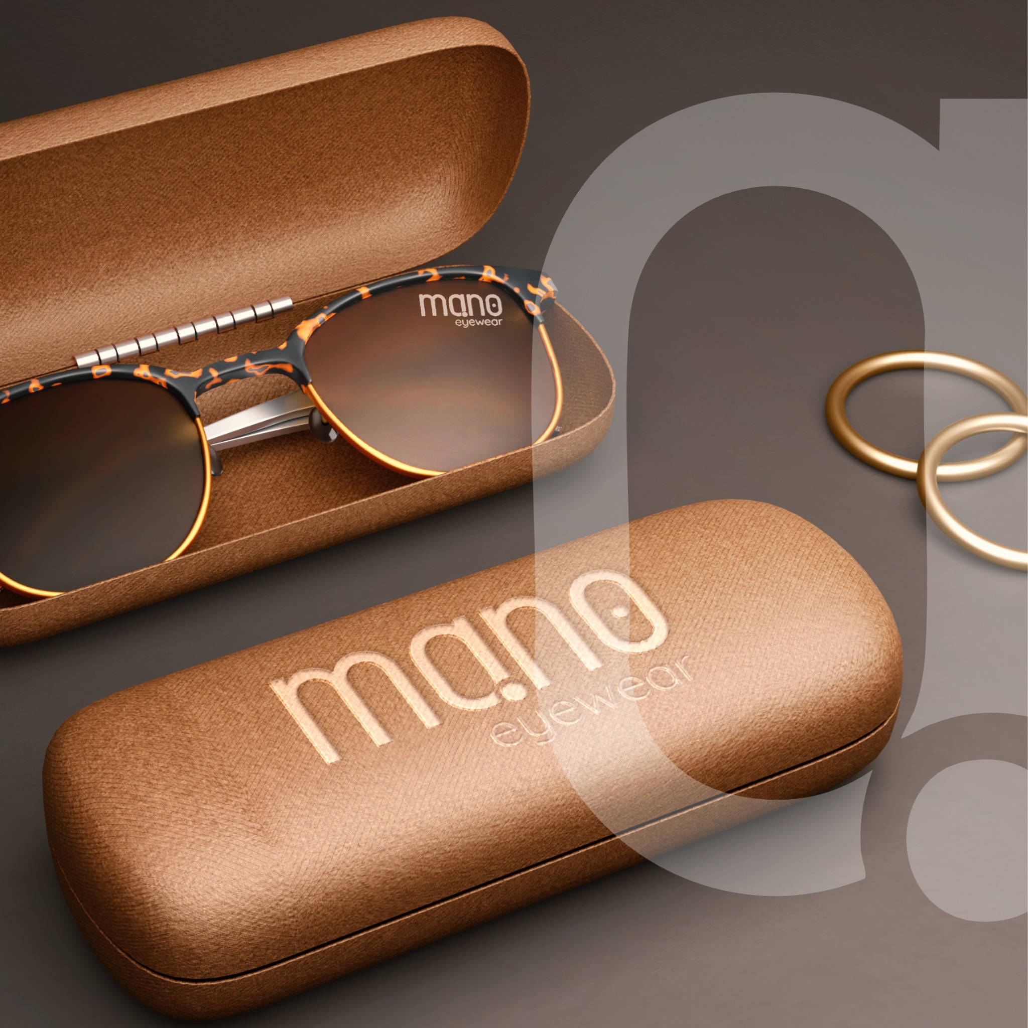 Okulary w brązowym etui z logo 'mano eyewear' obok złotych pierścieni na szarym tle.