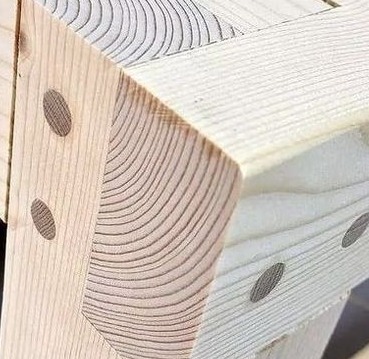 Detal narożnika konstrukcji drewnianej z widocznymi słojami i okrągłymi zaślepkami, jasne drewno w naturalnym oświetleniu.