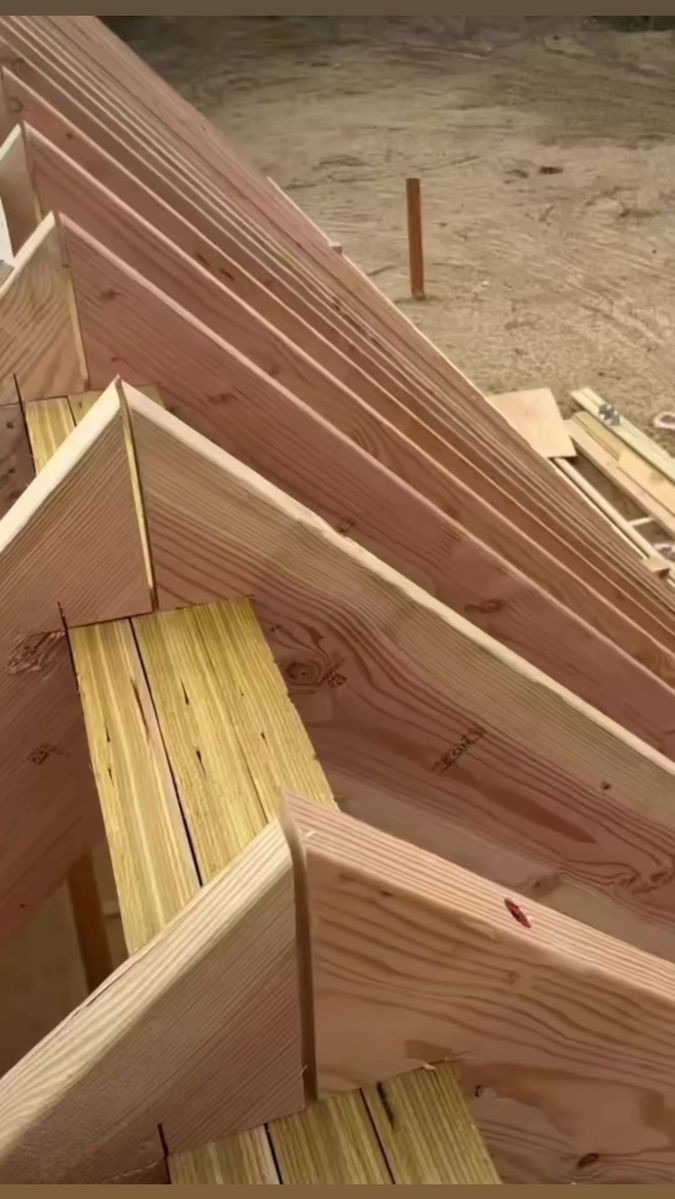 Konstrukcja drewniana dachu w trakcie budowy, widoczne krokwie i elementy nośne z jasnego drewna, surowy stan, tło stanowi piaszczysty teren.