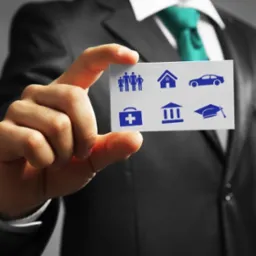 Mężczyzna w garniturze trzymający kartę z ikonami: rodzina, dom, samochód, apteczka, budynek z kolumnami, dyplom.