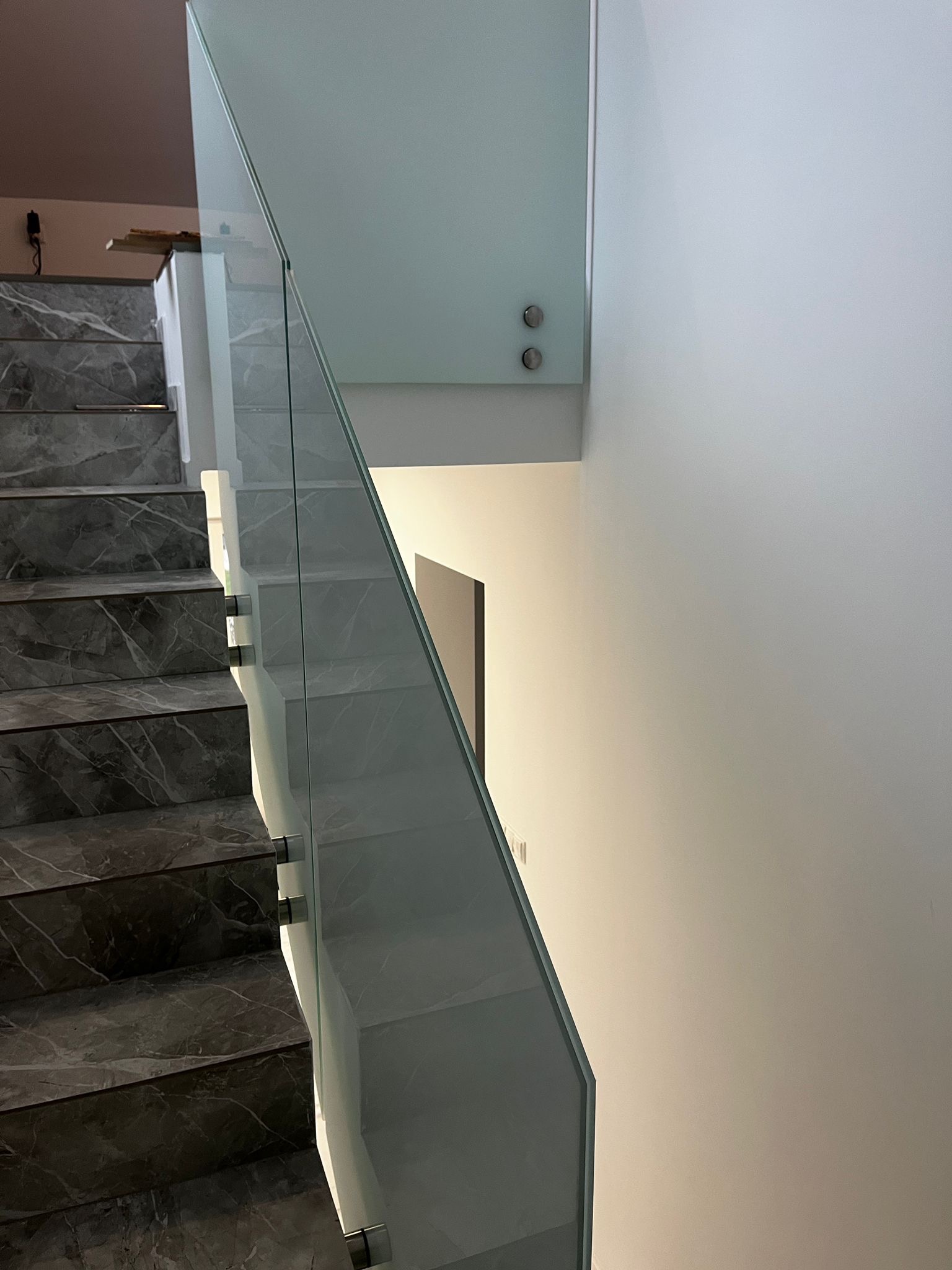 Marmurowe schody z nowoczesną szklaną balustradą, mocowaną punktowo. Minimalistyczny design, jasne wnętrze, widok z góry.