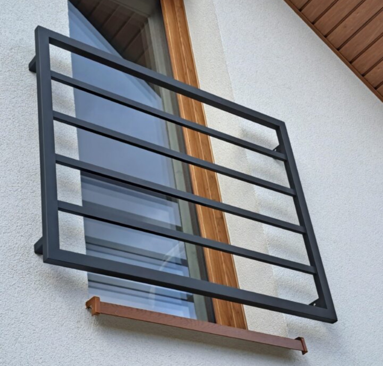 Czarna, metalowa krata okienna na elewacji budynku z oknem o drewnianych ramach. Minimalistyczny design, ochrona przed włamaniem, widok z zewnątrz.