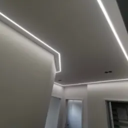 Nowoczesne oświetlenie LED wpuszczone w sufit, tworzące geometryczne linie światła w jasnym wnętrzu z widocznymi drzwiami.