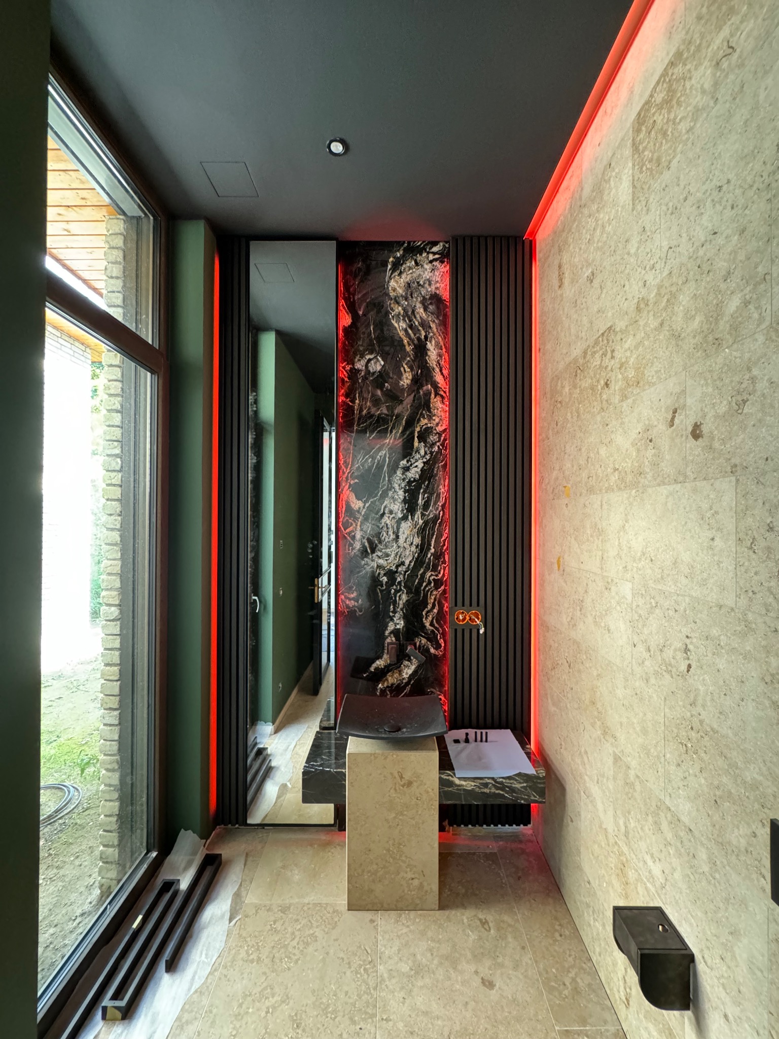 Nowoczesna łazienka z beżowymi płytkami na ścianach i podłodze, czarnym marmurem nad umywalką, oświetleniem LED i dużym oknem z widokiem na zewnątrz.