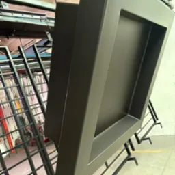 Metalowa rama po malowaniu proszkowym, zawieszona na wieszaku w hali produkcyjnej, widoczne ślady spawania na narożach.