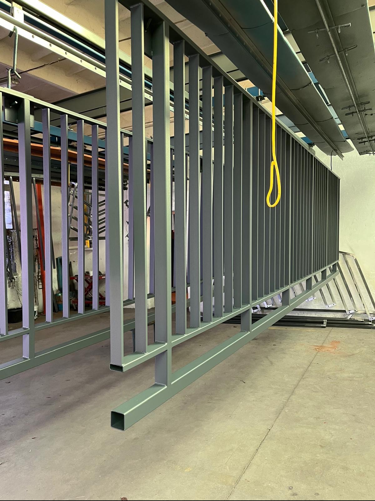 Szare metalowe balustrady po malowaniu, wiszący żółty przewód, surowy beton na podłodze i suficie.