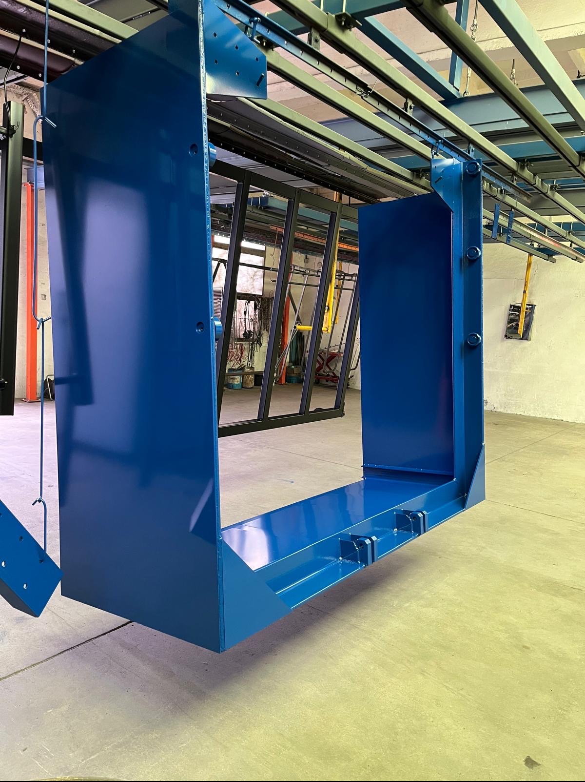 Element konstrukcyjny w kolorze niebieskim, zawieszony na systemie transportowym w hali produkcyjnej, po procesie malowania.