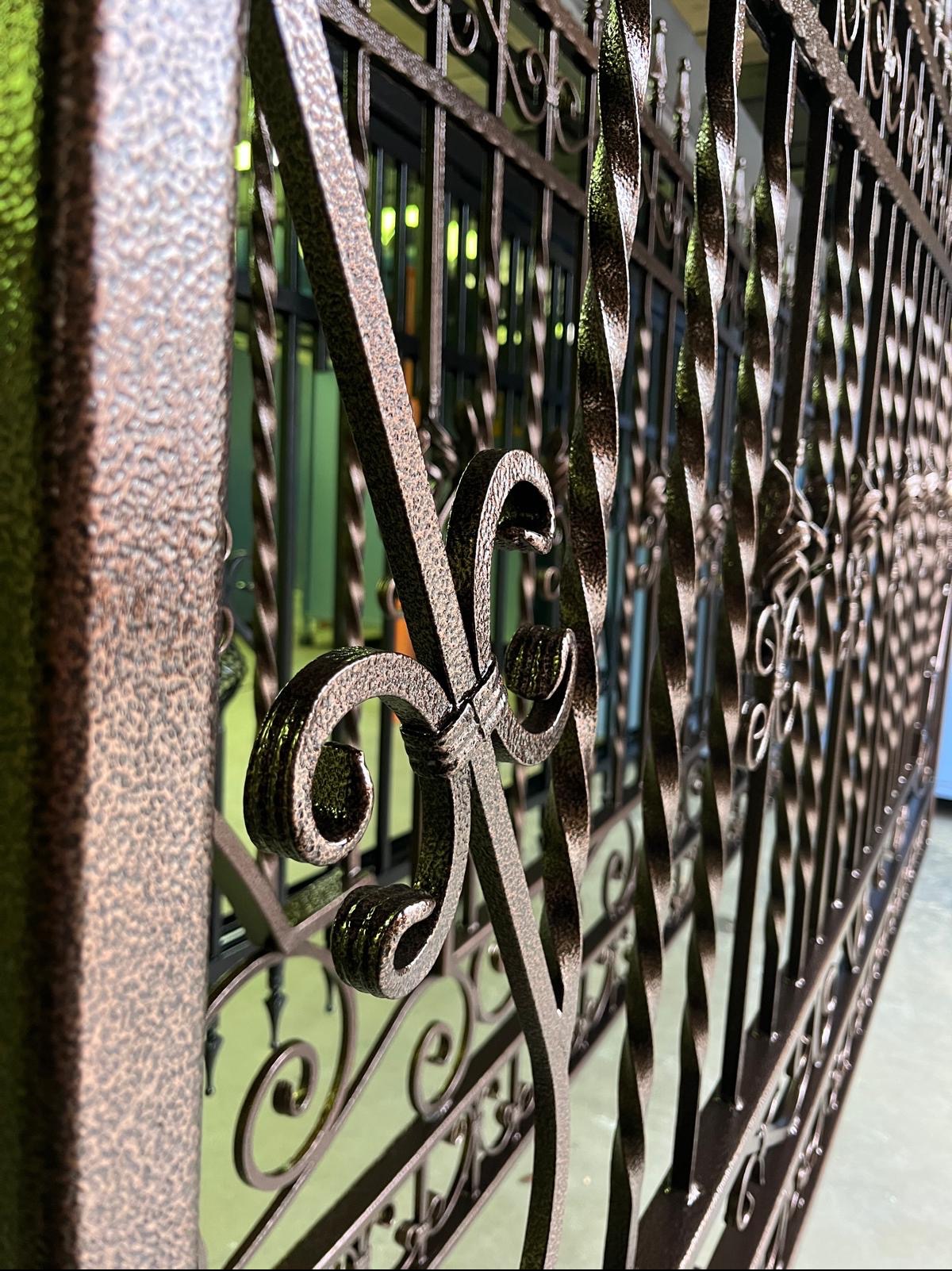 Metalowa brama z ozdobnymi elementami po obróbce, widoczna faktura powierzchni i detale spawów, brązowy odcień.