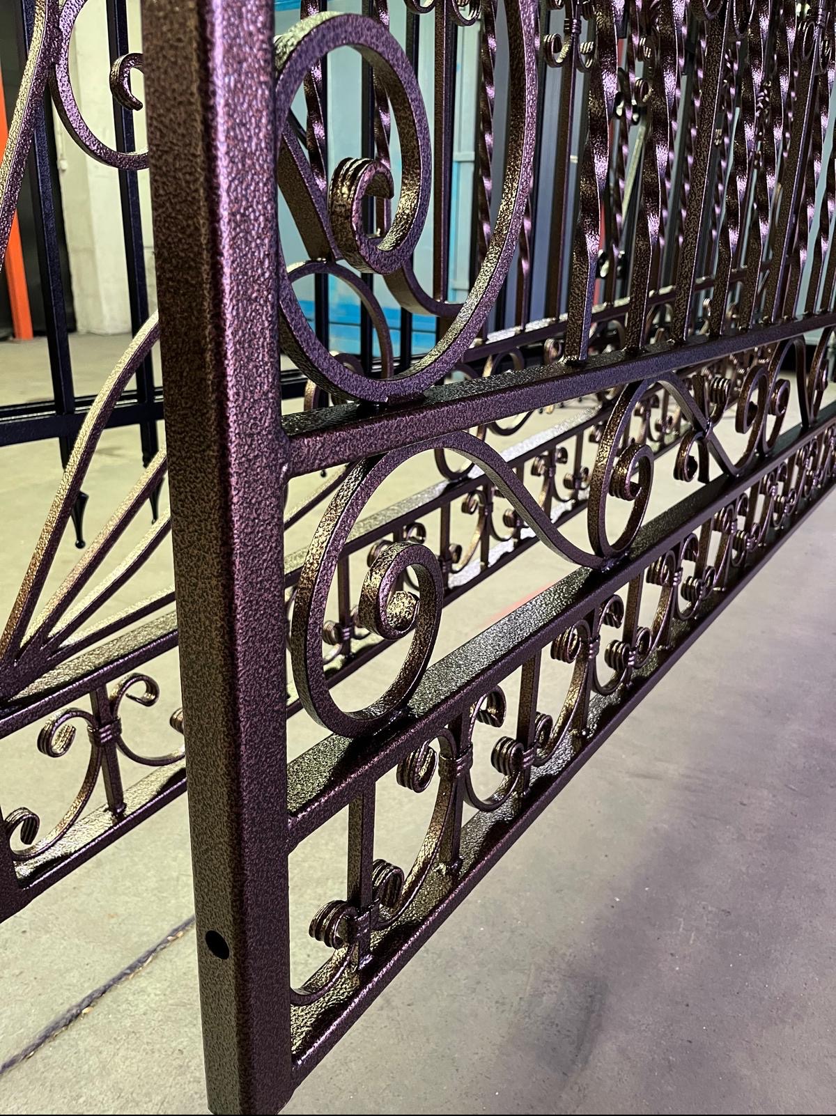 Fragment ozdobnej, metalowej bramy w kolorze brązowo-złotym, z widoczną fakturą powierzchni, po procesie malowania. Dekoracyjne, kręcone elementy. Widoczne spawania i łączenia elementów.