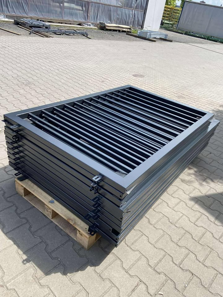 Stos pomalowanych na szaro metalowych przęseł ogrodzeniowych na palecie, widok z góry, kostka brukowa w tle, elementy ogrodzenia z poziomymi szczeblami.