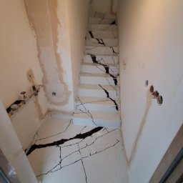 Bella Pietra - Montaż schodów kamiennych z białego marmuru z czarnymi żyłami w trakcie wykańczania wnętrza, widoczne niedoskonałości na ścianach i instalacje hydrauliczne.