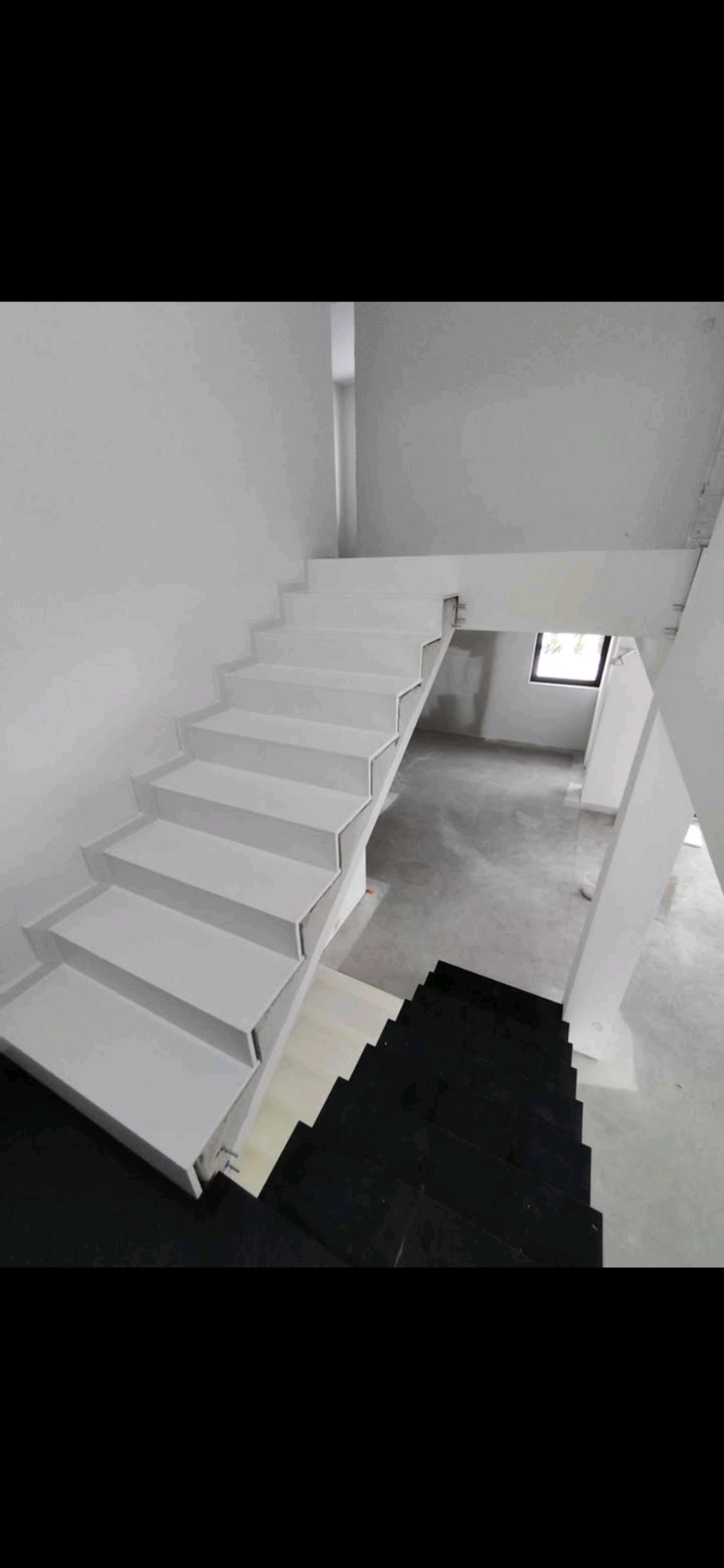 Nowoczesne, minimalistyczne schody wewnętrzne z białymi stopniami i czarnym podestem na dole, widoczne elementy konstrukcyjne, surowe wykończenie wnętrza.