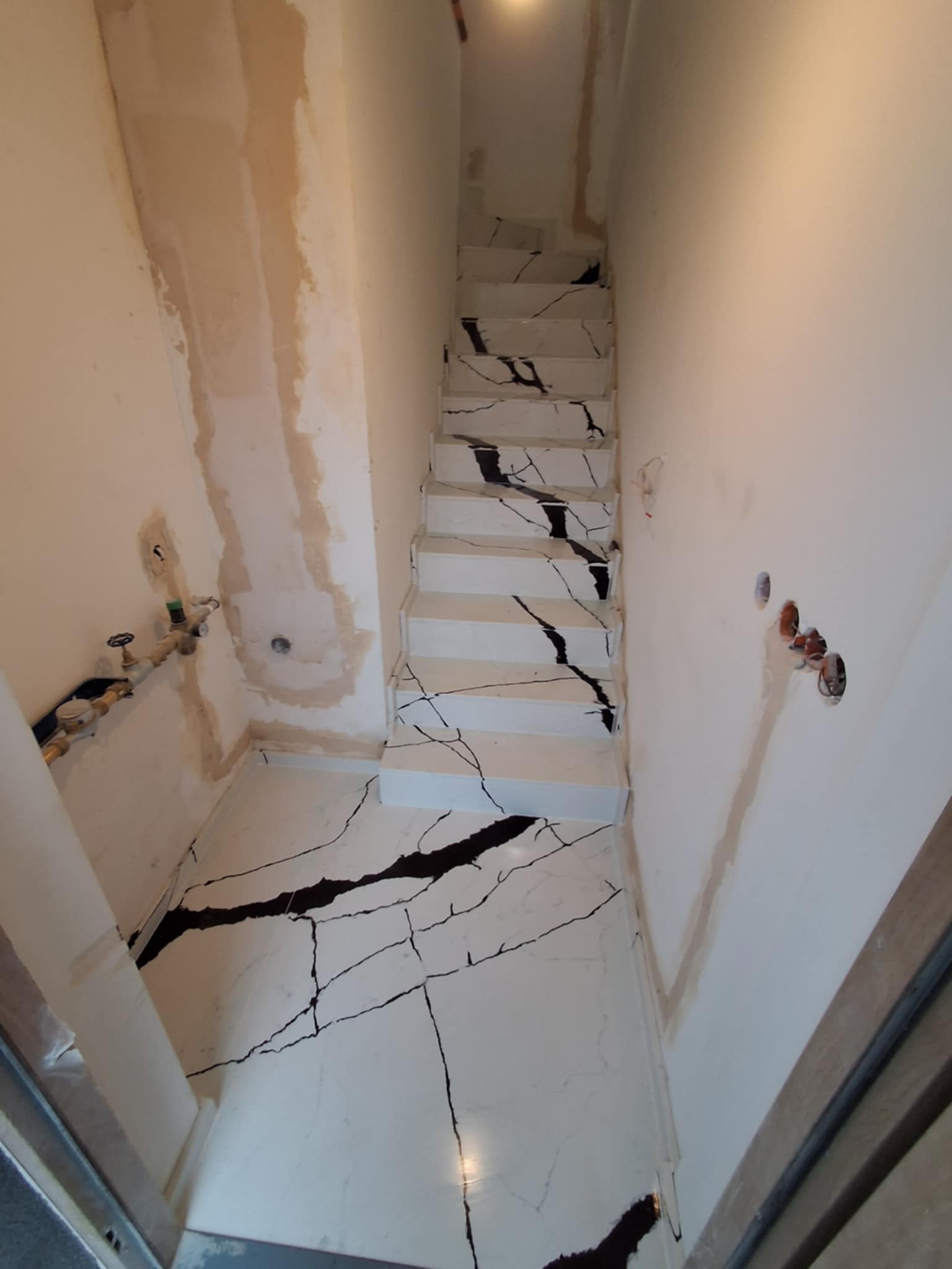 Montaż schodów kamiennych z białego marmuru z czarnymi żyłami w trakcie wykańczania wnętrza, widoczne niedoskonałości na ścianach i instalacje hydrauliczne.