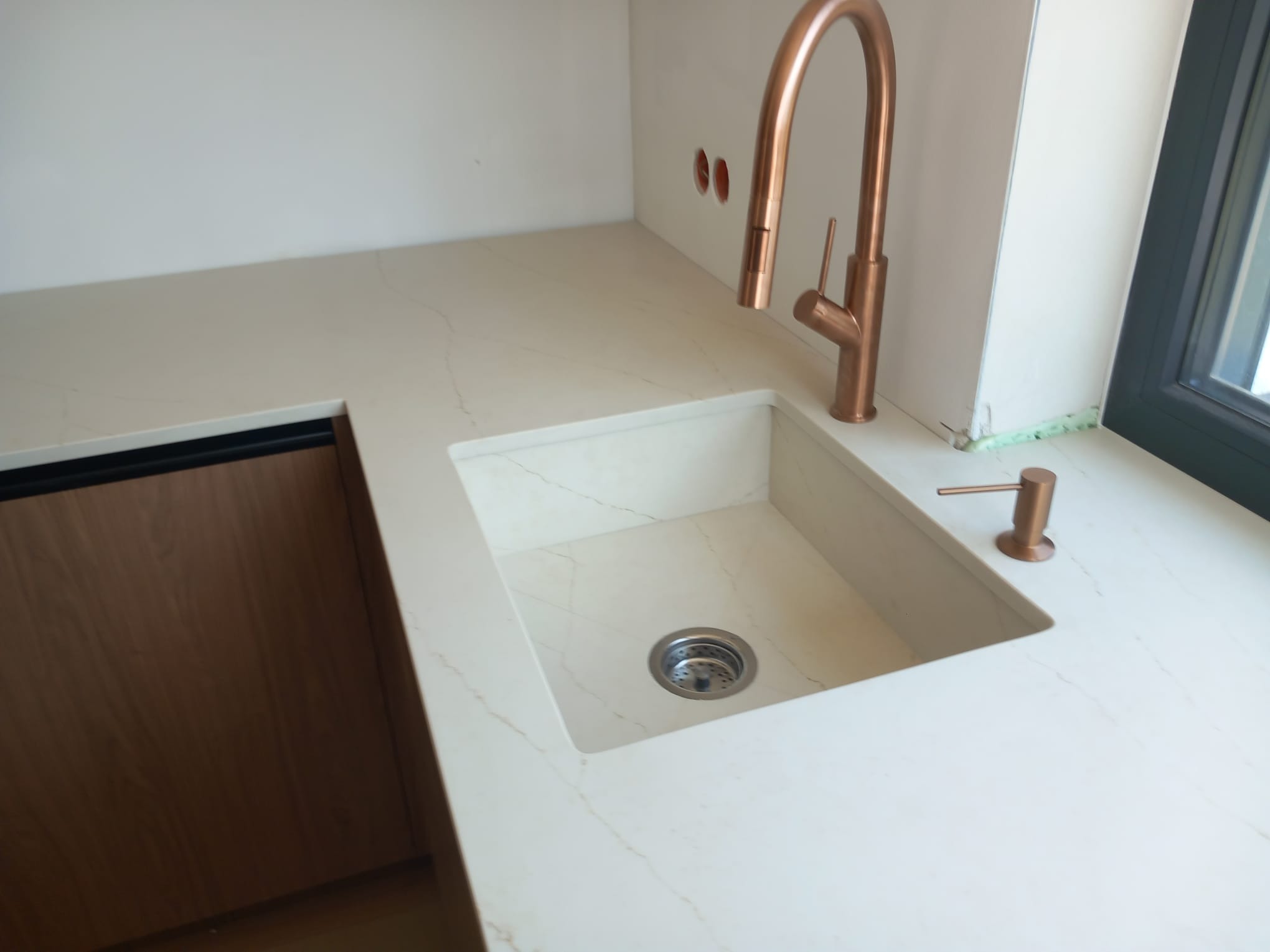 Beżowy blat kamienny z wbudowanym zlewozmywakiem i miedzianą baterią, widok z góry. Minimalistyczny design, subtelny wzór kamienia.