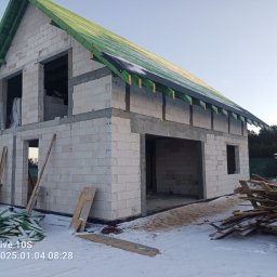 PERFECT HOUSE JAROSŁAW OPORSKI - Niedokończony budynek z białych bloczków, z zielonym dachem w trakcie budowy, widoczne deski i śnieg na ziemi, zarys samochodu w tle.