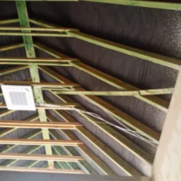 Konstrukcja dachu z widoczną membraną dachową, drewnianymi belkami pomalowanymi na zielono, przewodami elektrycznymi i zamontowaną klimatyzacją, widok z dołu.