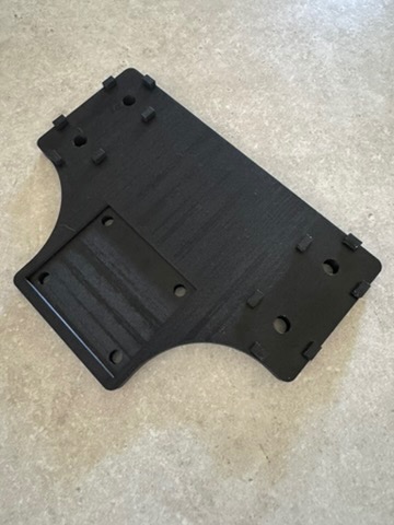 Czarny, nieregularny kształt z tworzywa z otworami i wypustkami, wykonany techniką druku 3D. Widoczne warstwy materiału i struktura powierzchni.