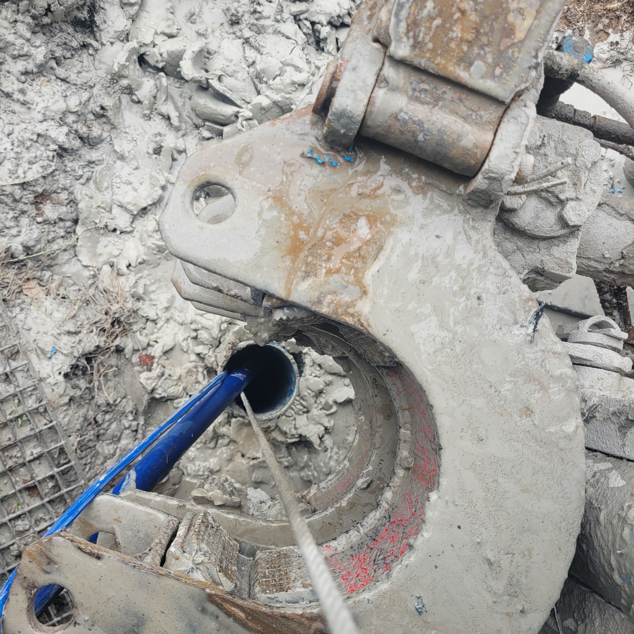 Wiertnica w trakcie pracy, widoczny fragment rury w otworze, otoczenie pokryte błotem i resztkami urobku.