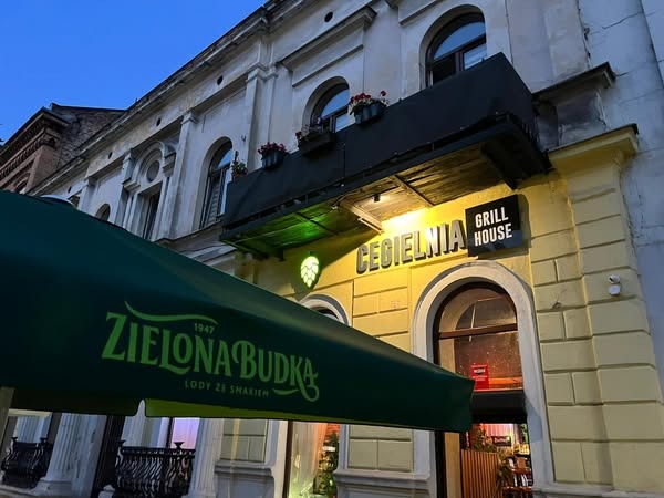 Oświetlony budynek Cegielni Grill House nocą, z zielonym baldachimem ZIELONA BUDKA. Widoczne detale architektoniczne i oświetlenie zewnętrzne.