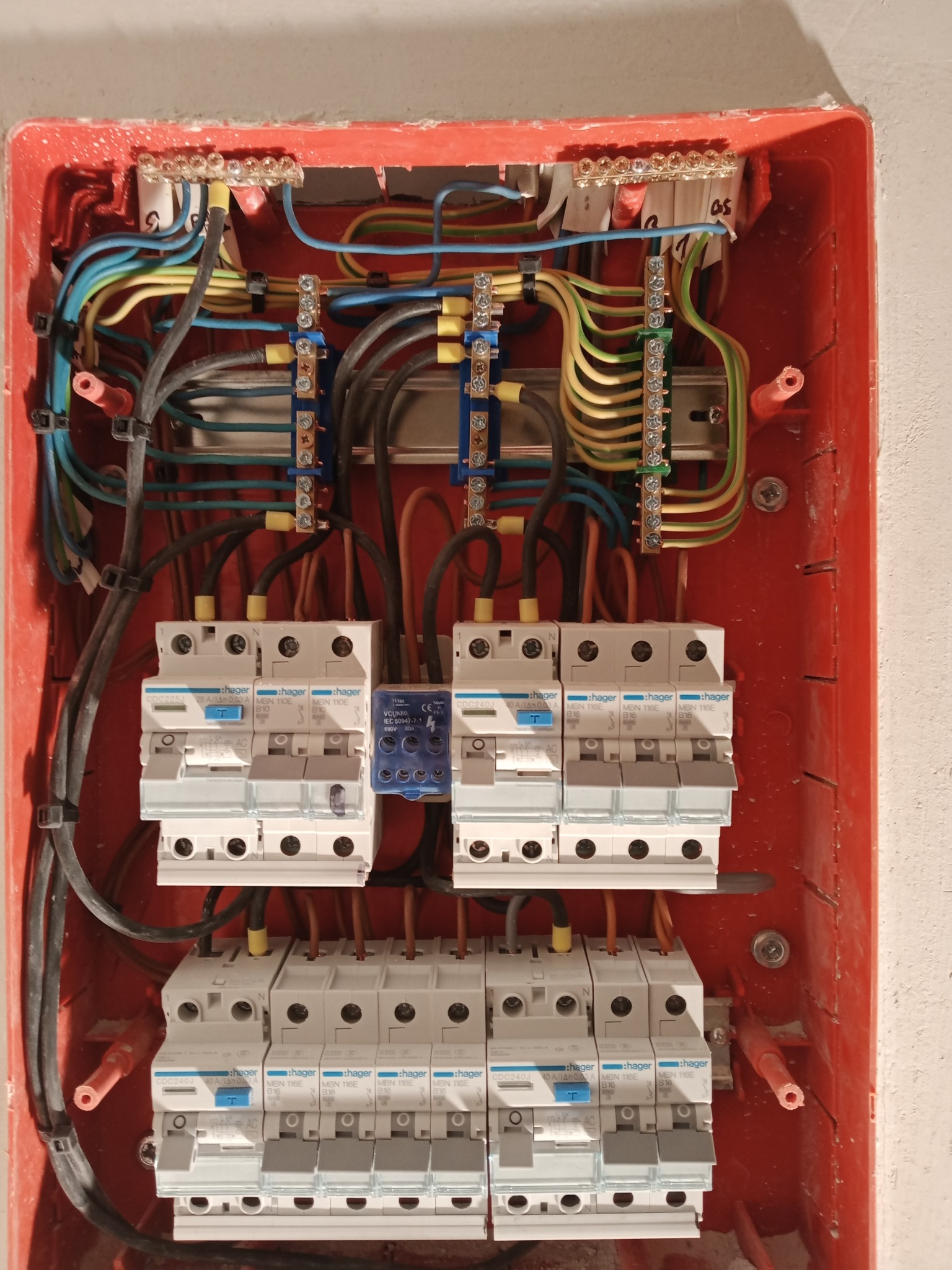Rozdzielnia elektryczna Hager w czerwonej obudowie. Widoczne bezpieczniki, przewody i listwy zaciskowe. Instalacja w trakcie montażu, wnętrze skrzynki z bliska.