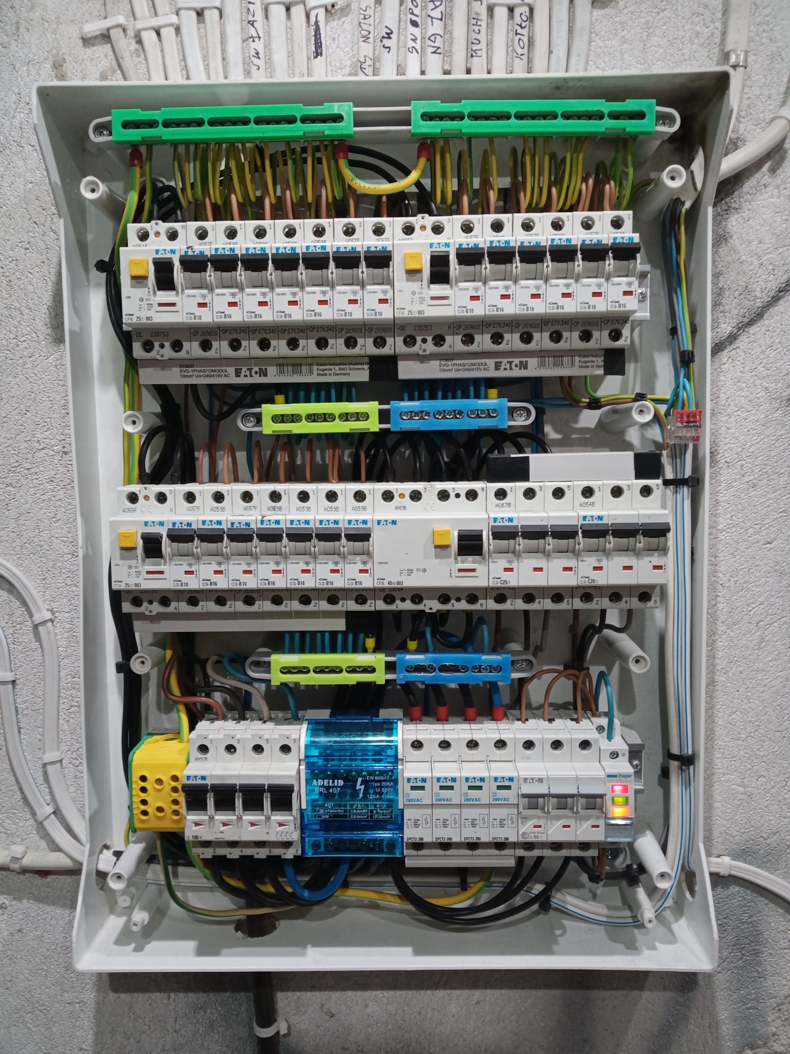 Otwarta skrzynka elektryczna z zainstalowanymi bezpiecznikami i okablowaniem, widoczne elementy marki Eaton i Hager. Instalacja schludna, w białej obudowie.