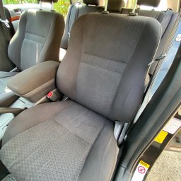 Tomasz Czernik - Wnętrze samochodu w Porębie z widocznymi, lekko zabrudzonymi, tekstylnymi siedzeniami i podłokietnikiem. Fotel kierowcy z widocznym pasem bezpieczeństwa, a w tle kolejne rzędy siedzeń.