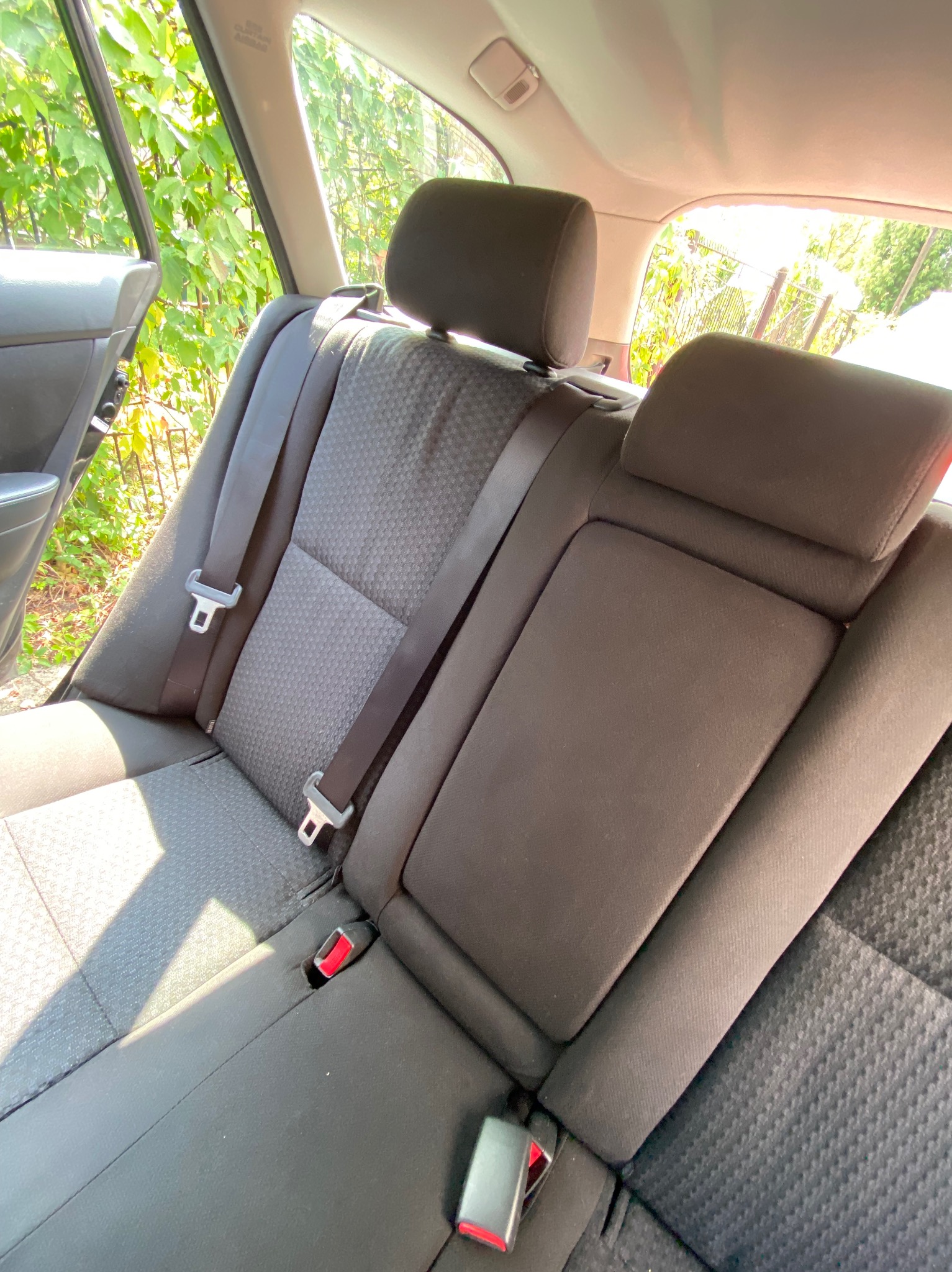 Wnętrze samochodu: tylna kanapa z widocznymi pasami bezpieczeństwa i zagłówkami, z delikatnym cieniem padającym na tapicerkę.