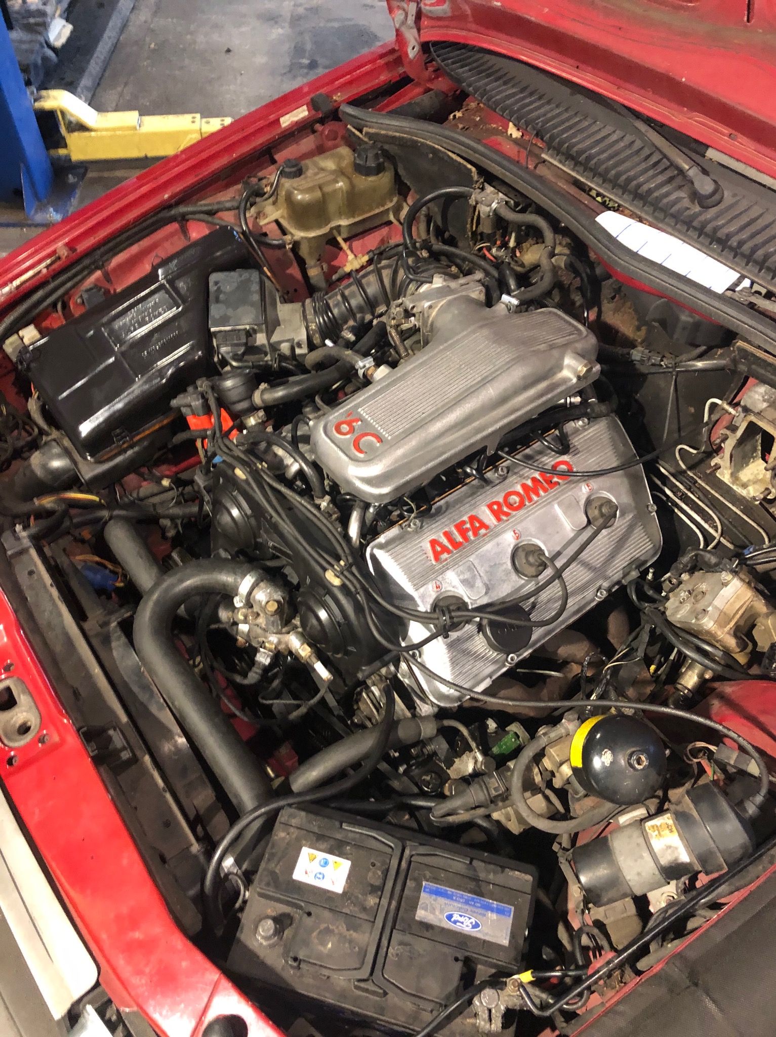 Otwarta maska czerwonego samochodu Alfa Romeo, ukazująca szczegółowy widok silnika 6C z elementami osprzętu.