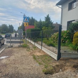 ŚLĄSKIE CENTRUM OGRODZEŃ TOMASZ BUCKI - Nowoczesne ogrodzenie panelowe z podmurówką betonową, widok z zewnątrz posesji. Słupki w kolorze grafitowym. W tle zieleń i zabudowa jednorodzinna.