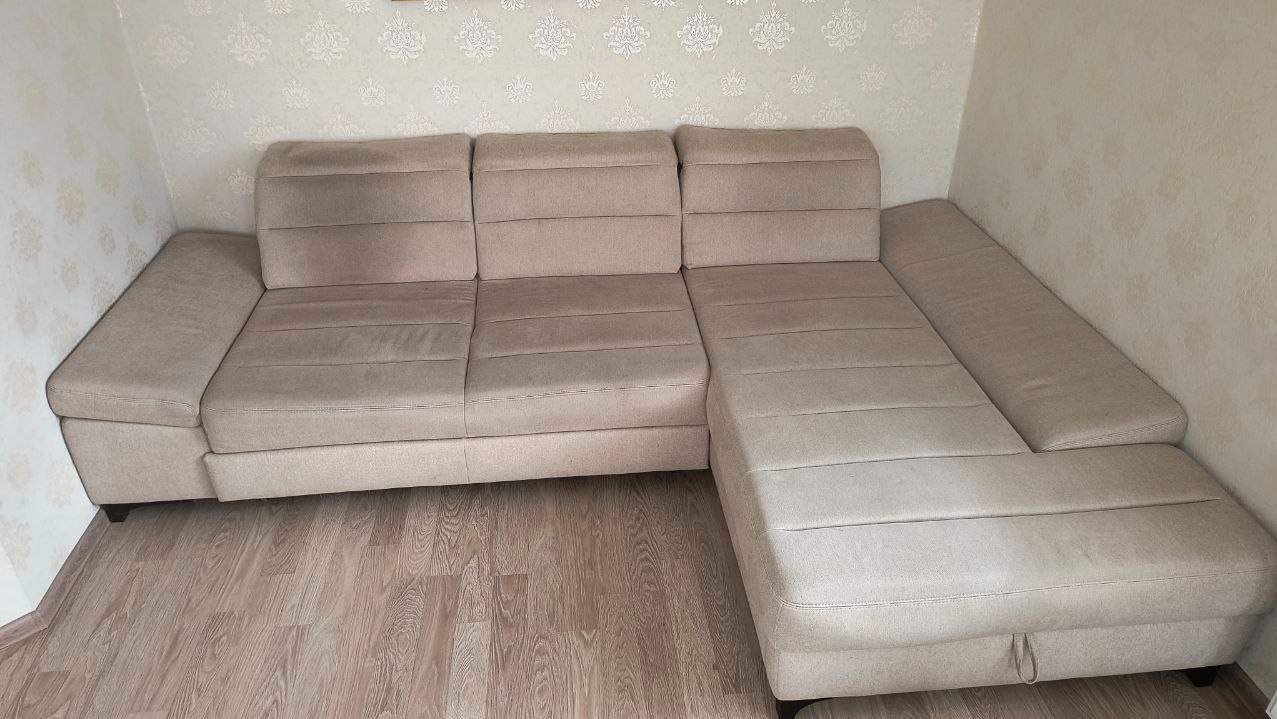 Beżowy narożnik z widocznymi plamami na siedzisku i oparciu, stojący na drewnianej podłodze w pokoju z tapetą w delikatne wzory.