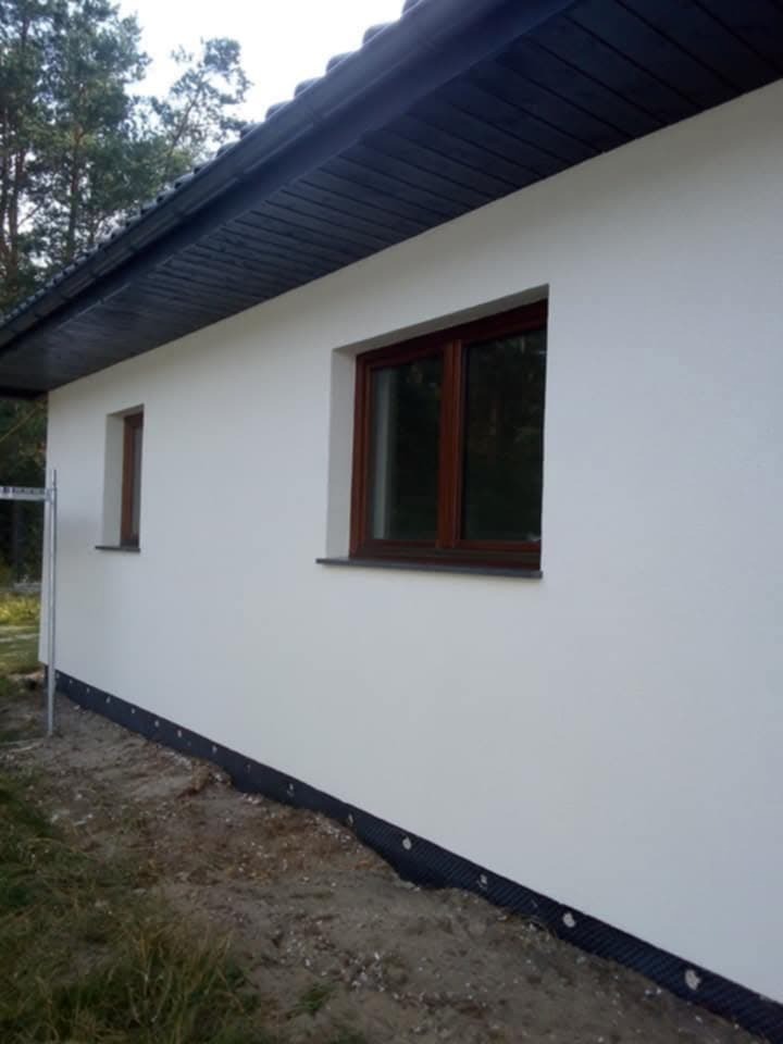 Świeżo otynkowana elewacja domu jednorodzinnego w Unisławiu, z widoczną listwą startową i drewnianymi oknami.