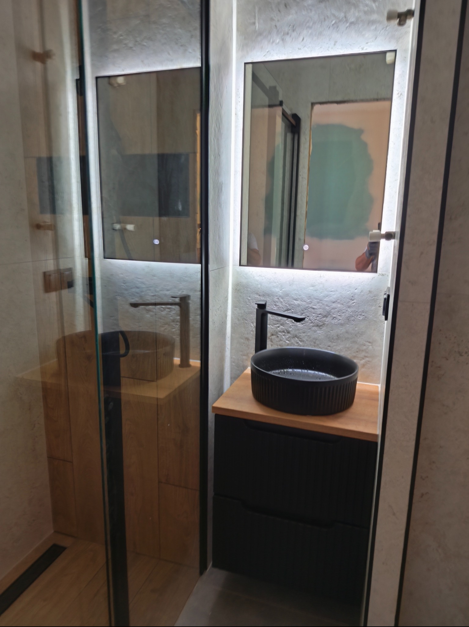 Nowoczesna łazienka z kabiną prysznicową, umywalką nablatową i podświetlanym lustrem. Minimalistyczny design, szaro-beżowa kolorystyka, drewniane akcenty.